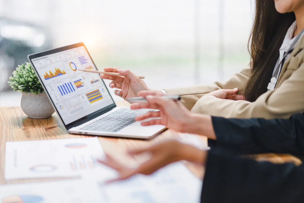 Two professional analyzing financial data graphs, charts on laptop display at a modern workspace. Financial analysis or business evaluation concept
