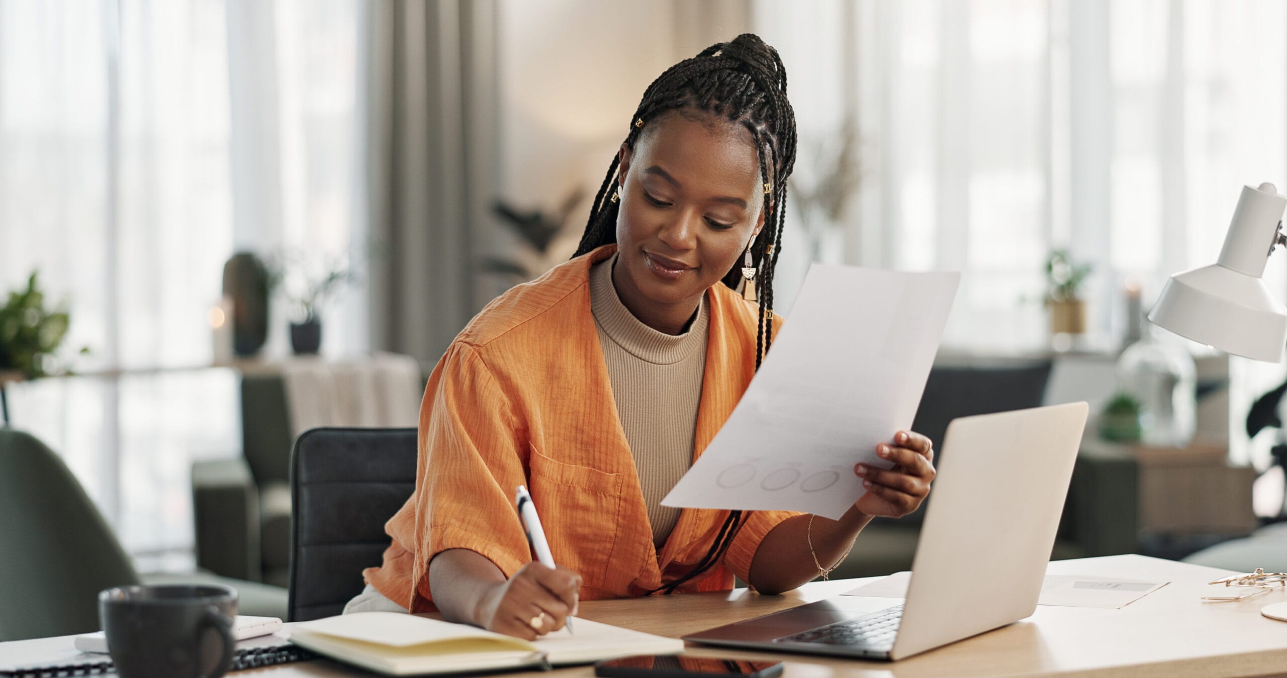 Black woman in home office, documents and laptop for research in remote work, ideas and thinking. Happy girl at desk with computer, writing notes and online search in house for freelance networking.