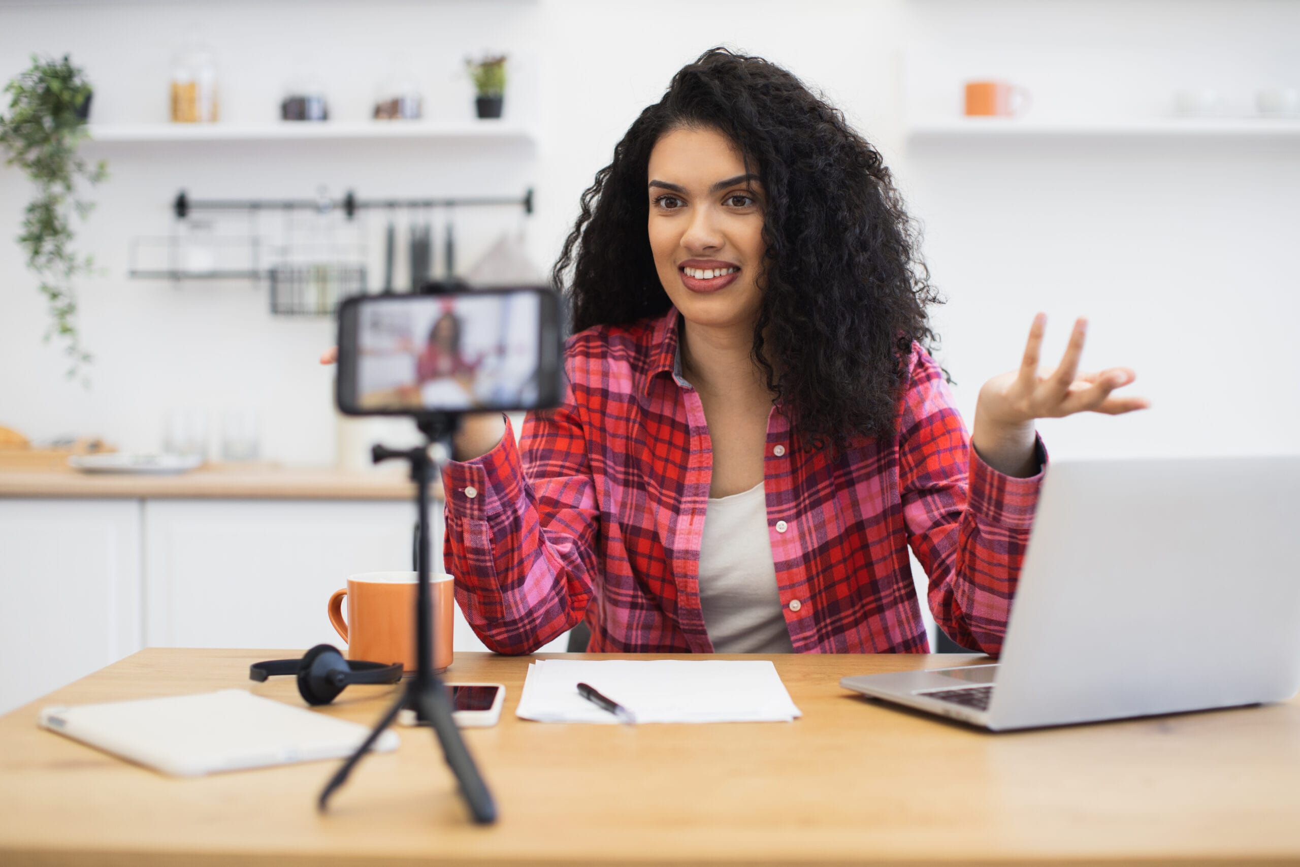 Young woman recording vlog at home using smartphone and laptop